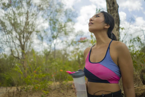Outdoors lifestyle portrait of young attractive tired and thirsty Asian woman drinking water after hard running workout cooling off at beautiful green park — Stock Photo, Image