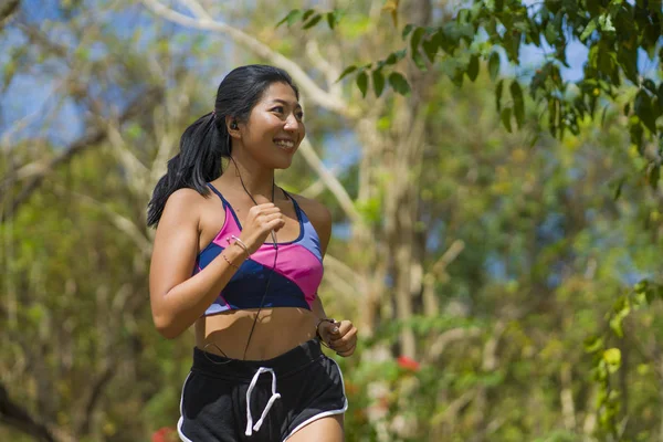 Joven feliz atractivo y exótico asiático indonesio corredor mujer en trotar entrenamiento al aire libre en campo camino pista naturaleza fondo corriendo alegre — Foto de Stock