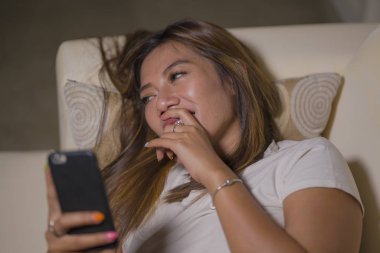 genç çekici mutlu ve rahat öğrenci kız cep telefonu gülümseyerek internet sosyal medya veya flört uygulaması kullanarak oturma odası kanepede ev keyfi