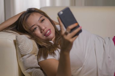 genç çekici mutlu ve rahat öğrenci kız cep telefonu gülümseyerek internet sosyal medya veya flört uygulaması kullanarak oturma odası kanepede ev keyfi