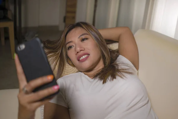 젊은 매력적인 행복하고 편안한 학생 아시아 여자 즐기는 홈리 거짓말 에 거실 소파 소파 를 사용하여 인터넷 소셜 미디어 또는 휴대 전화에 데이트 응용 프로그램 — 스톡 사진
