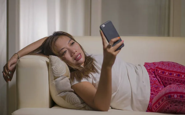 Jeune attrayant heureux et détendu étudiant asiatique femme appréciant confortable couché sur canapé salon en utilisant les médias sociaux Internet ou sortir ensemble app sur téléphone mobile — Photo