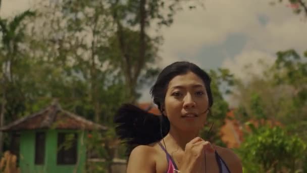 若いエキゾチックなフィット感とスポーツと健康的なライフスタイルの概念でジョギングワークアウトを行うアスファルト道路を走る美しいアジアのインドネシアの女性のドリースタイルでジンバルショットを引き戻します — ストック動画