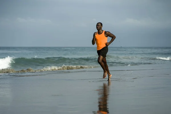 athletic full body portrait of young attractive and fit black afro American man running on the beach doing Summer fitness jogging workout at the sea in healthy lifestyle concept