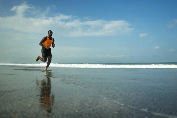 Athletic full body portrait of young attractive and fit black afro American man running on the beach doing Summer fitness jogging workout at the sea in healthy lifestyle concept — Stock Photo, Image