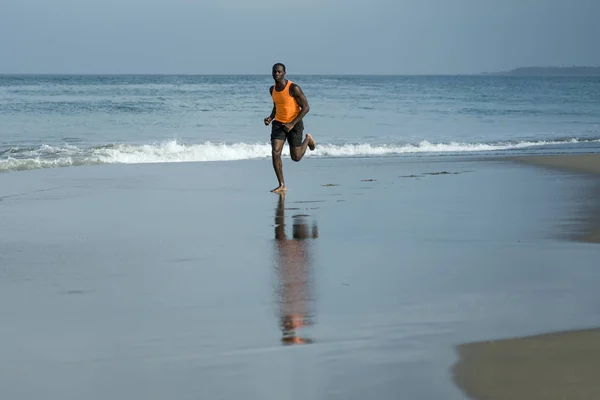 Athletic full body portrait of young attractive and fit black African American man running on the beach doing Summer fitness jogging workout at the sea in healthy lifestyle — Stock Photo, Image
