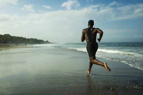Athletic full body portrait of young attractive and fit black African American man running on the beach doing Summer fitness jogging workout at the sea in healthy lifestyle — Stock Photo, Image