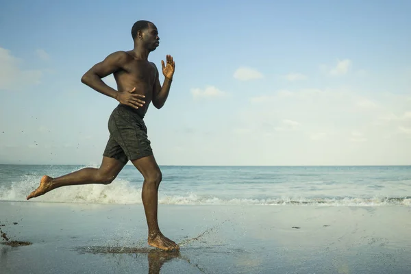 athletic full body portrait of young attractive and fit black African American man running on the beach doing Summer fitness jogging workout at the sea in healthy lifestyle