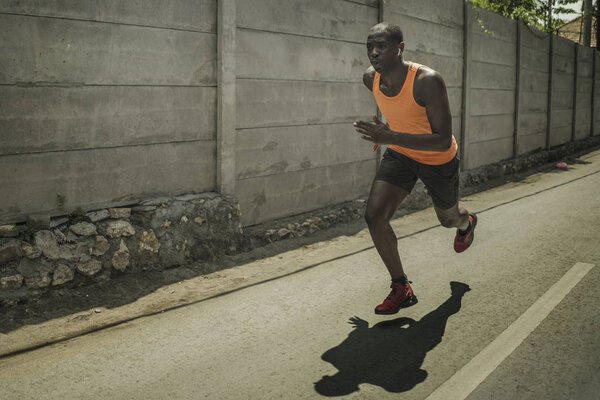 городской бегун тренировки. Молодой привлекательный и атлетичный чернокожий афроамериканец бегает на улице по асфальтовым дорогам, тренируя тяжелую пробежку в спорте и здоровом образе жизни
