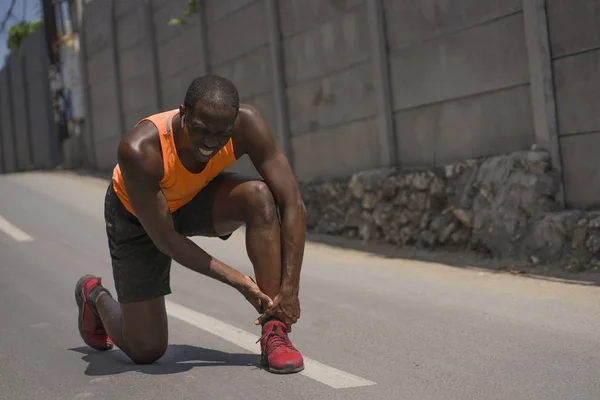 Junger, athletischer und fitter afroamerikanischer Läufer mit Schmerzen, der sein Sprunggelenk hält, nachdem er medizinische Probleme mit einer Sehnen- oder Bänderverletzung während des städtischen Lauftrainings hatte — Stockfoto