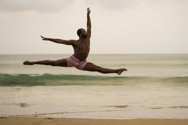 çağdaş dans koreograf bale plaj egzersiz yapıyor . genç çekici ve atletik siyah Afrikalı-Amerikalı adam gün doğumunda dans zarif atlama