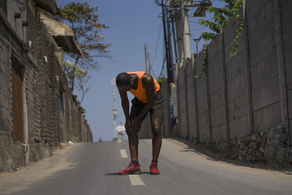 молодой атлетичный и здоровый черный афро-американский бегун, страдающий от боли в колене после травмы сухожилий или связок во время бега по городу
