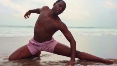 Çağdaş bale dansçısı plajda sahne yapıyor. Gimbal genç çekici ve atletik siyah Afrikalı Amerikalı adam deniz tarafından dans vurdu