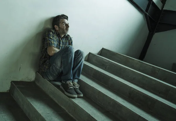 Dramatický portrét mladého depresivní a paranoidního muže sedícího venku na tmavém, nevzrušeným rohu schodiště, které pociťuje nemoc z deprese a úzkostná krize — Stock fotografie