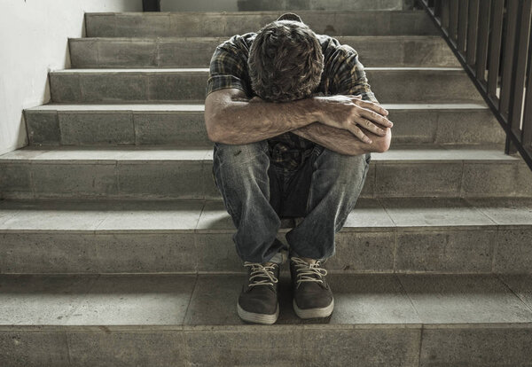 отчаянный человек, сидящий на улице на темной гранж-стрит лестнице, чувствуя себя больным, страдающим депрессией и тревожным кризисом в концепции психического здоровья
