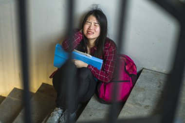 Dramatic portrait of Asian female college student bullied. Young depressed and sad Japanese girl sitting lonely on campus staircase suffering bullying and harassment clipart