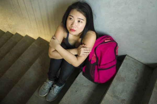 Retrato dramático de una estudiante universitaria asiática acosada. Joven chica japonesa deprimida y triste sentada sola en la escalera del campus sufriendo intimidación y acoso — Foto de Stock