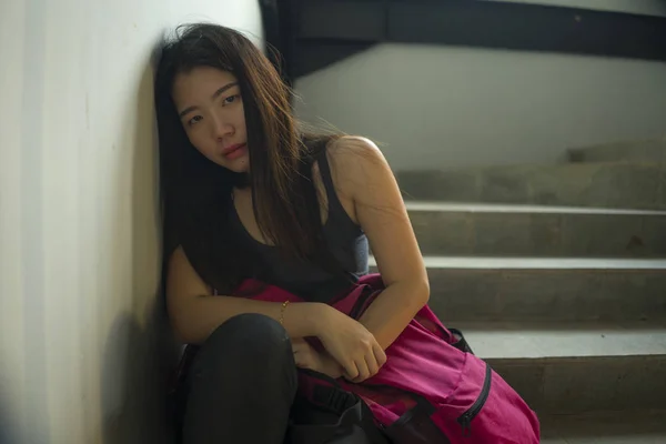 Retrato dramático de una estudiante universitaria asiática acosada. Joven chica coreana deprimida y triste sentada sola en la escalera del campus sufriendo intimidación y acoso —  Fotos de Stock