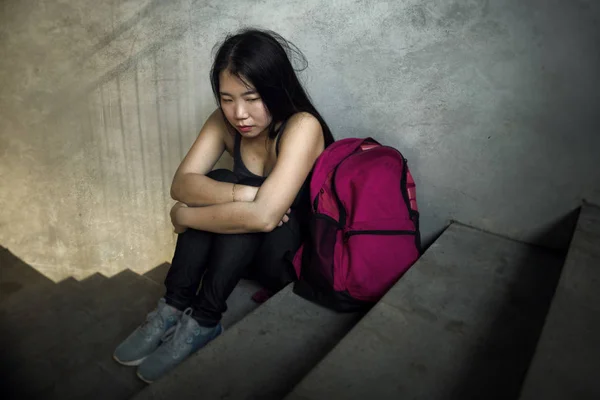 Retrato dramático de una estudiante universitaria asiática acosada. Joven chica coreana deprimida y triste sentada sola en la escalera del campus sufriendo intimidación y acoso —  Fotos de Stock