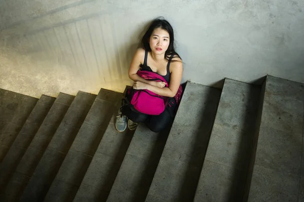 Retrato dramático de una estudiante universitaria asiática acosada. Joven deprimida y triste chica china sentada sola en la escalera del campus sufriendo intimidación y acoso — Foto de Stock