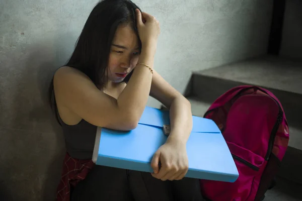 Retrato dramático de una estudiante universitaria asiática acosada. Joven deprimida y triste chica china sentada sola en la escalera del campus sufriendo intimidación y acoso —  Fotos de Stock