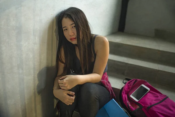 Драматический портрет азиатской студентки колледжа. Молодая депрессивная и грустная японская девушка, одиноко сидящая на лестнице кампуса, страдает от издевательств и преследований. — стоковое фото