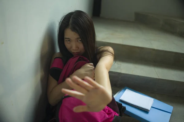 Молодая красивая депрессивная азиатская студентка колледжа, сидящая на лестничной клетке кампуса, жертва жестокого обращения, чувствующая себя испуганной и одинокой. — стоковое фото