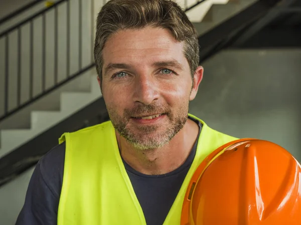 Corporate Portrait von jungen attraktiven und glücklichen Bauarbeiter Mann oder Bauunternehmer posiert selbstbewusst lächelnd mit Bauhelm und Weste in blauem Kragen Job Lifestyle — Stockfoto