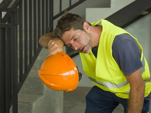 Porträt eines attraktiven und erschöpften Bauarbeiters in Helm und Weste auf der Baustelle, der während eines anstrengenden Arbeitstages durchatmet, verschwitzt und müde — Stockfoto