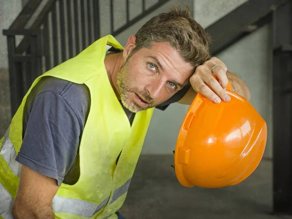 Portret van aantrekkelijk en uitgeput bouwvakker in helm en vest op bouwplaats het nemen van een adem tijdens een harde werkdag alle zweterig en moe — Stockfoto