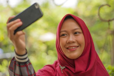 Müslüman öğrenci yaşam tarzı - genç güzel mutlu ve neşeli Asya Endonezya öğrenci kız İslam geleneksel başörtüsü başörtüsü cep telefonu ile selfie alarak giyiyor