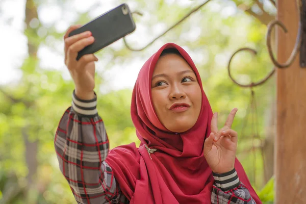 Estilo de vida estudantil muçulmano - jovem bela menina estudante asiática feliz e alegre Indonésia vestindo Islã tradicional hijab cabeça cachecol tomando selfie com telefone celular — Fotografia de Stock