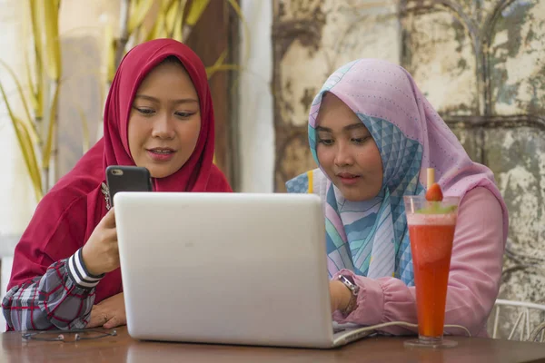 Молодые счастливые и красивые мусульманские студентки в традиционном исламском хиджабе голову шарф говорить онлайн бизнес, работая вместе в кафе с ноутбуком — стоковое фото