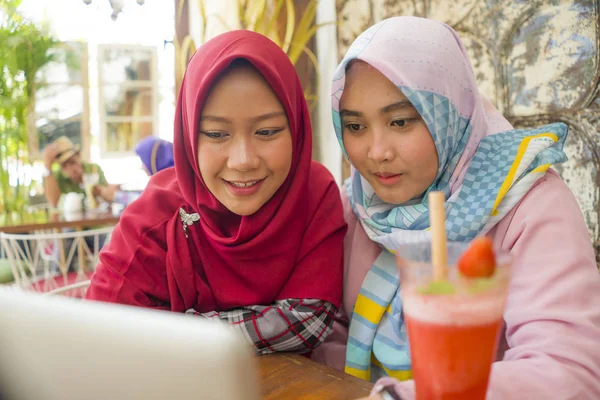 Молодые счастливые и красивые мусульманские студентки в традиционном исламском хиджабе голову шарф говорить онлайн бизнес, работая вместе в кафе с ноутбуком — стоковое фото