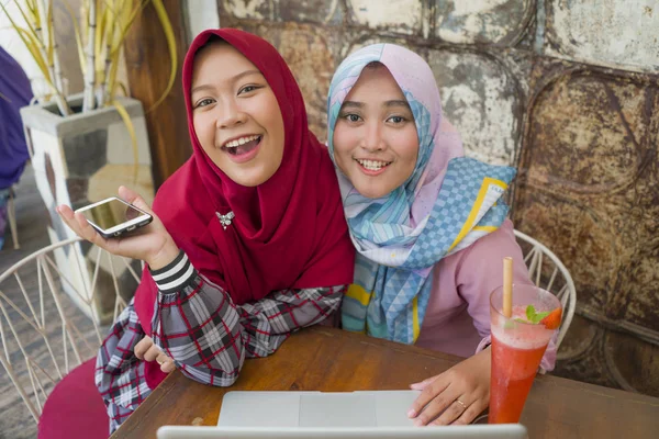 Jóvenes mujeres estudiantes musulmanes felices y hermosas en la bufanda tradicional islámica hijab cabeza hablando de negocios en línea trabajando juntos en la cafetería con ordenador portátil — Foto de Stock