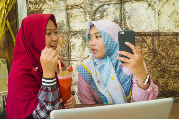 Jóvenes mujeres estudiantes musulmanes felices y hermosas en la bufanda tradicional islámica hijab cabeza hablando de negocios en línea trabajando juntos en la cafetería con ordenador portátil — Foto de Stock