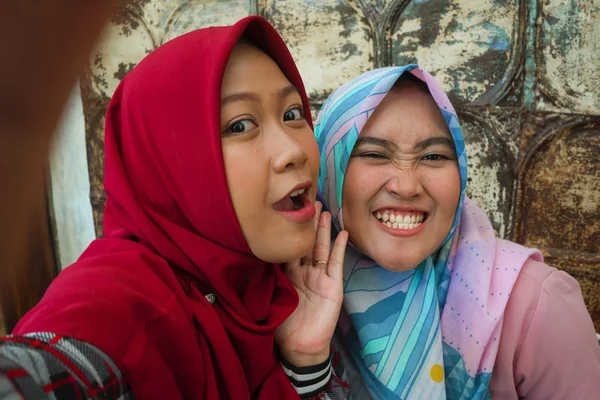 伝統的なイスラムヒジャーブヘッドスカーフで幸せでかわいいアジアのインドネシアの女の子は、友情とソーシャルメディアの概念でカフェで楽しんで一緒に自分撮りを取ります — ストック写真