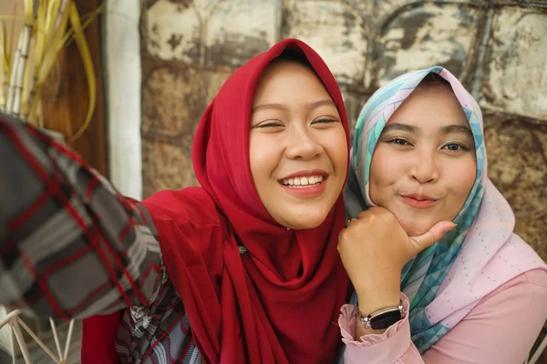 Meninas indonésias felizes e bonitas no tradicional lenço de cabeça hijab islâmico tirando selfie juntos se divertindo no café em amizade e conceito de mídia social — Fotografia de Stock