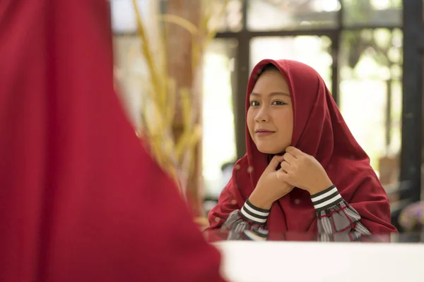 Mirror reflection of young happy and beautiful Muslim woman in traditional hijab adjusting red head scarf in beauty and fashion concept smiling in sweet face expression — Stock Photo, Image