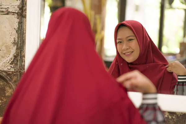 Espelho reflexo de jovem mulher muçulmana feliz e bonita no tradicional hijab ajustando lenço cabeça vermelha em conceito de beleza e moda sorrindo na expressão do rosto doce — Fotografia de Stock