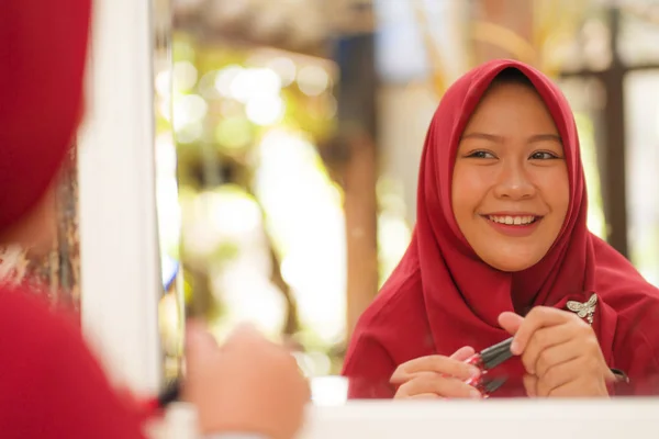 Miroir reflet de jeune femme musulmane heureuse et belle dans le foulard traditionnel hijab tête appliquant maquillage et cosmétiques poupées gaies dans le concept de la beauté et de la mode — Photo