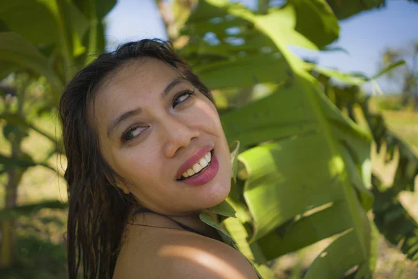 Young beautiful and happy Asian Indonesian woman in bikini posing between leaves of banana tree smiling natural isolated on exotic tropical background in Summer holiday — Stock Photo, Image