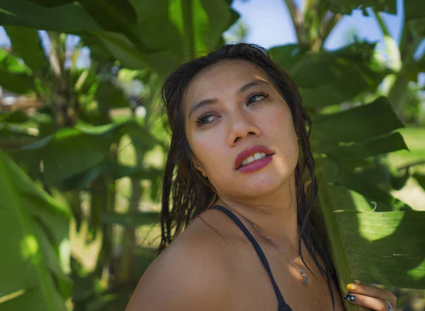 Joven hermosa y feliz asiática indonesia mujer en bikini posando entre hojas de plátano sonriendo natural aislado en exótico tropical fondo en vacaciones de verano —  Fotos de Stock