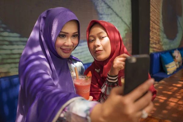 Mulher muçulmana e sua filha adolescente. Menina indonésia asiática feliz tomando selfie com sua bela mãe tanto no tradicional lenço cabeça hijab islâmico juntos no café — Fotografia de Stock