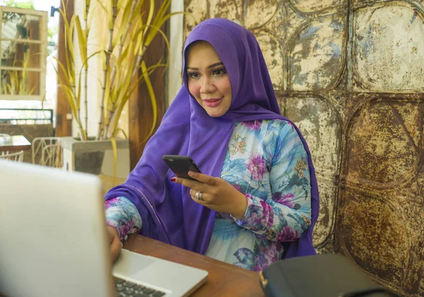 Jonge mooie en succesvolle Aziatische vrouw in traditionele hijab hoofd sjaal werken op laptop computer en mobiele telefoon Running online Internet Business ontspannen en gelukkig — Stockfoto