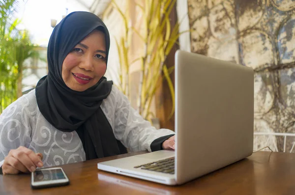 Mezza età asiatico indonesiano musulmano donna in hijab tradizionale testa sciarpa lavoro rilassato a casa giardino in esecuzione business online in internet successo di lavoro — Foto Stock