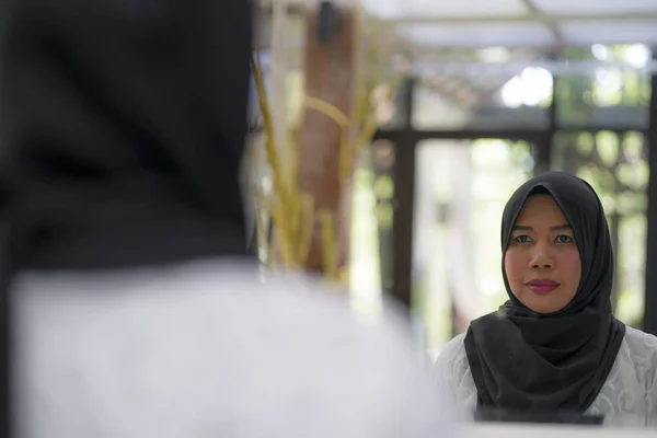 Retrato de estilo de vida de mulher muçulmana indonésia asiática de meia-idade elegante e feliz em hijab tradicional ajustando o lenço islâmico na frente do espelho — Fotografia de Stock