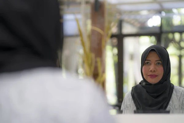 Estilo de vida retrato de mujer musulmana indonesia asiática de mediana edad elegante y feliz en hiyab tradicional ajustando la bufanda islámica frente al espejo — Foto de Stock