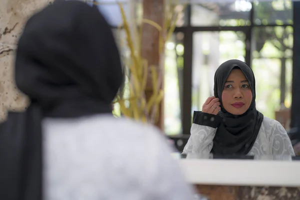 Estilo de vida retrato de mujer musulmana indonesia asiática de mediana edad elegante y feliz en hiyab tradicional ajustando la bufanda islámica frente al espejo — Foto de Stock