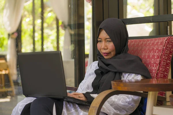 Estilo de vida retrato de meia idade asiático indonésio muçulmano mulher no tradicional hijab cabeça cachecol trabalhando relaxado em casa executando negócios on-line no sucesso do trabalho na internet — Fotografia de Stock